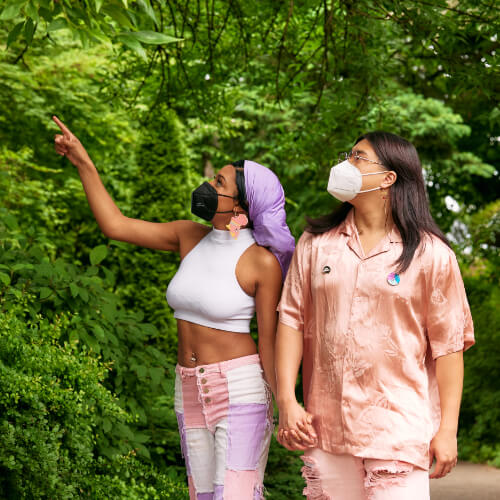 A masked autistic Black and Asian couple point out park sights on a date.