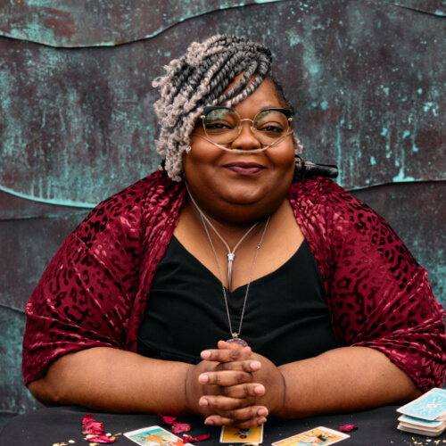 A Black woman with a nasal cannula smiling with hands loosely folded.