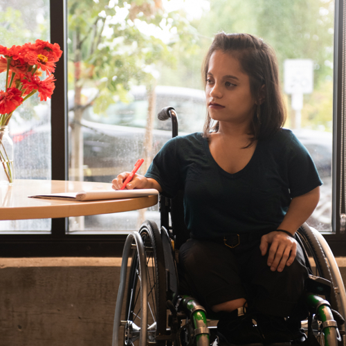 A South Asian person sits in a wheelchair and gazes off-camera.