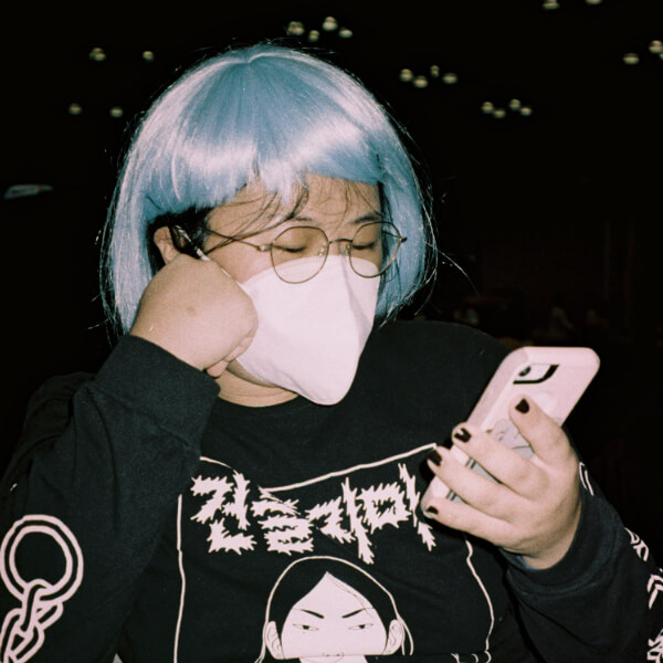 A masked East Asian person with glasses looks at their phone.